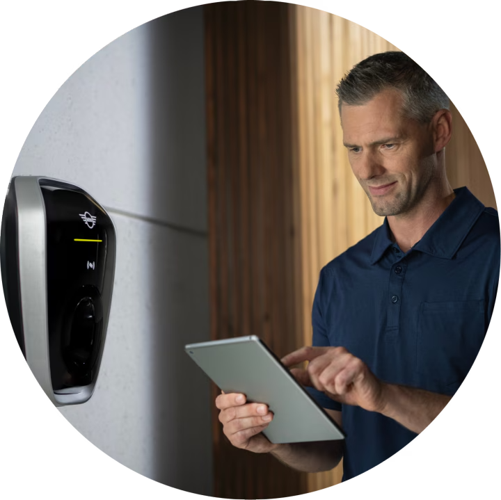 A man looks down at an iPad while standing in front of a home charging device.