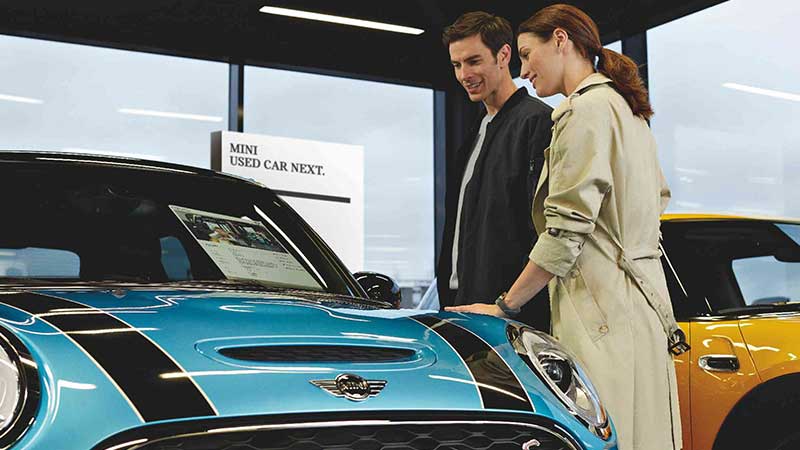 A man and women smiling down at a MINI at a dealership.